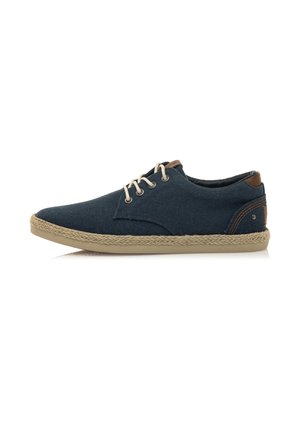 Zapatilla de lona azul con suela de cuerda beige, punta redonda y acentos marrones en dos tonos. Presenta tres ojales con cordones claros y parte superior texturizada.