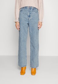 Vide ben som skjerf i lys blått, med høy midje og klassisk fem-lommers design, parret med klare gule blokkhelte mules.