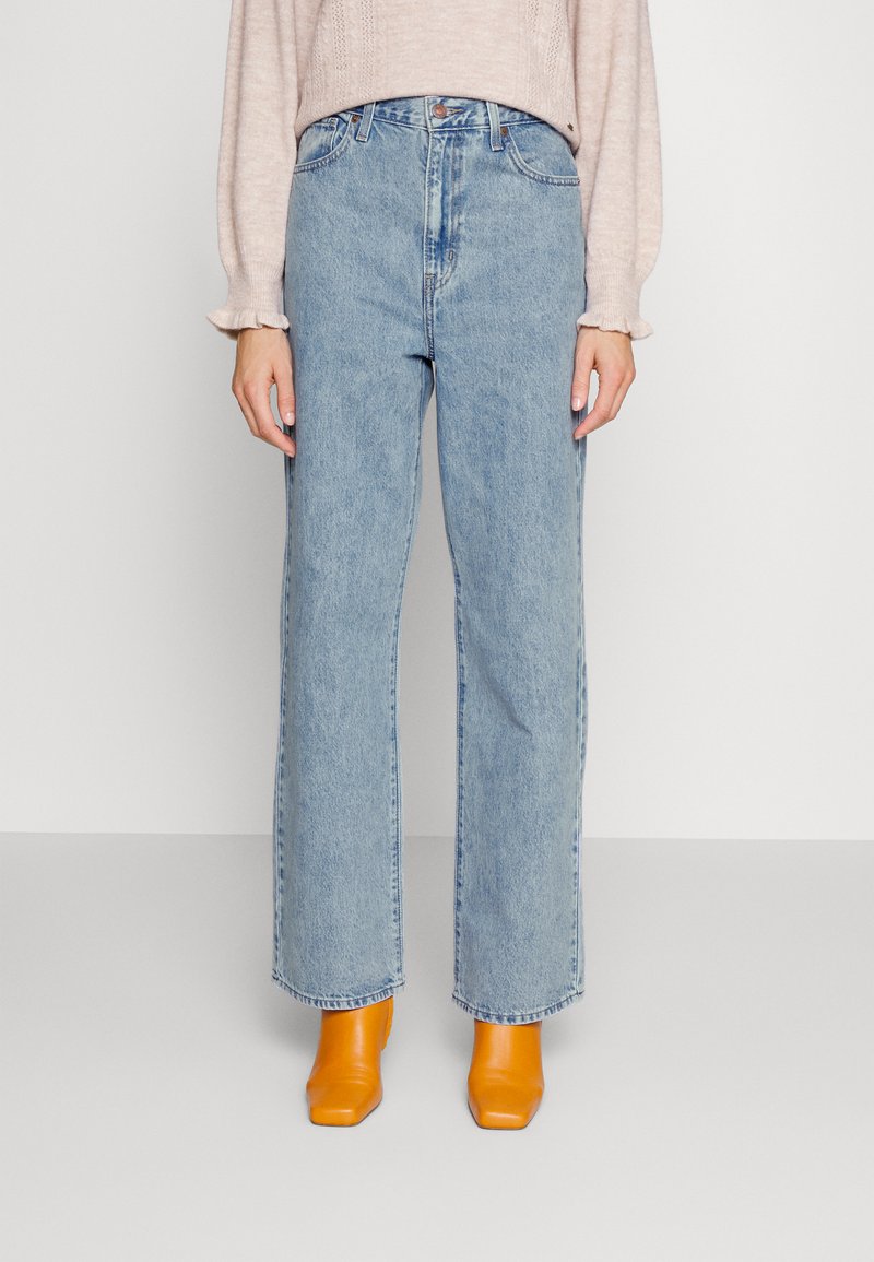 Vide ben som skjerf i lys blått, med høy midje og klassisk fem-lommers design, parret med klare gule blokkhelte mules.