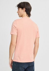 Camiseta de manga corta de color rosa claro, hecha de tejido suave, con cuello redondo y un corte holgado, con una etiqueta visible en el dobladillo.