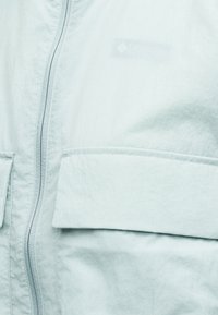 Κοντινή λήψη γαλάζιου μπουφάν που δείχνει το εμπρόσθιο φερμουάρ και τη μεγάλη τσέπη με καπάκι από υφασμάτινη υφή.