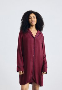 Abito da pigiama in satin borgogna con strisce verticali, colletto a punte, maniche lunghe e piping blu lungo i bordi. Bottoni sul davanti.