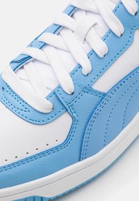 Jasnoniebieski sneaker z syntetycznej skóry z białymi sznurowadłami i akcentami, charakteryzujący się teksturowanym wzorem oraz perforacjami na przedniej części buta.