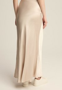 Sukienka midi z satyny w jasnym beżu, z gładką fakturą i dopasowanym pasem, zestawiona z beżowymi trampkami na codzienną stylizację.