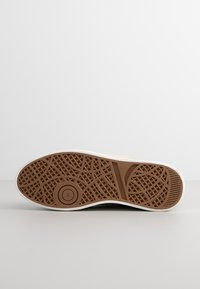 Suola in gomma per sneaker con una superficie marrone texturizzata e un bordo bianco. Presenta motivi intricati per la presa e include dettagli di branding.