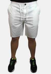 Pantaloni corti bianchi con cintura elastica, cordino e due tasche laterali. Tessuto morbido, lunghezza fino al ginocchio, abbinati a scarpe sportive nere con accenti neon.