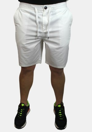 Pantaloni corti bianchi con cintura elastica, cordino e due tasche laterali. Tessuto morbido, lunghezza fino al ginocchio, abbinati a scarpe sportive nere con accenti neon.