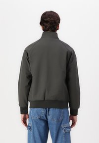 Giacca pullover grigia scura con colletto alto e polsini a coste, realizzata in un materiale morbido. Presenta maniche raglan e un design corto.