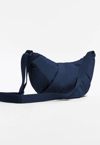 Sac bandoulière rembourré bleu marine avec un design incurvé, en tissu texturé et une sangle tissée. Présente une surface lisse et un matériel minimal.