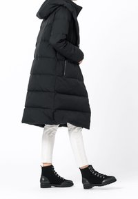 Svart uppblåsbar jacka med huva och quiltat mönster, ihop med åtsittande vita byxor och svarta snörstövlar.