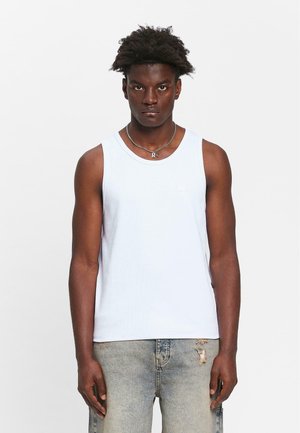 Hvit bomulls tanktopp med ribbestruktur, med rund hals og en liten logo detalj. Brukt sammen med lyseblå slitte jeans.