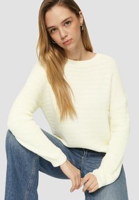 Pull crème côtelé avec un décolleté large et une coupe décontractée, associé à un jean bleu. La texture est douce avec un léger motif horizontal.