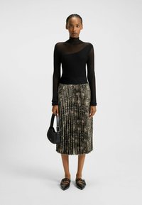 Czarna, ribbed turtleneck z asymetrycznym wzornictwem, zestawiona z plisowaną spódnicą w serpentynowy nadruk w ziemistych odcieniach, uzupełniona czarnymi płaskimi butami i torebką.