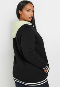 Schwarze Kapuzenjacke mit hellgrüner Innenausstattung, gestreiften Bündchen und Saum, seitlichen Taschen und einem lässigen Schnitt.