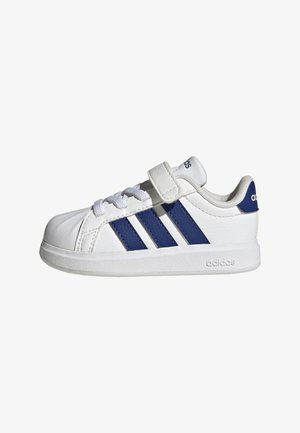 Witte Adidas sneaker met blauwe strepen, veters en een klittenbandsluiting, gezien vanaf de zijkant op een witte achtergrond.