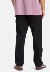 Čierne bavlnené nohavice s voľným strihom, ktoré majú dve zadné vrecká. Skombinované s hnedými a bielymi pruhovanými sandálmi. Košeľa je svetlofialová.