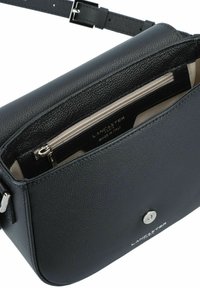 Black leather crossbody bag with a textured finish, top zip closure, interior zip pocket, and a silver logo on the front. Adjustable strap.