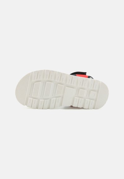 Zapatilla negra y roja con una suela de goma blanca texturizada. Cuenta con una forma redondeada, un diseño robusto y un patrón de banda distintivo para mejorar la tracción.
