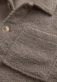 Grau strukturiertes Wollmischgewebe mit aufgesetzter Tasche und Knopfverschluss, mit weichem, flauschigem Aussehen.