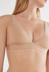 Světle béžový bezdrátový bralet s hlubokým výstřihem do V, bezešvým designem, širokým podkasaním a hladkou texturou. Ideální pro pohodlí a vrstvení.