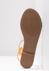 Gul sandal med flad sål, der har en tekstureret brun gummibund og et tyndt stropdesign. Størrelse 38 angivet på bunden.
