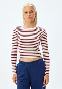 Korte mouwen crop top, wit met bordeauxrode horizontale strepen. Zacht materiaal, ronde halslijn. Gecombineerd met blauwe broek met elastische taille.