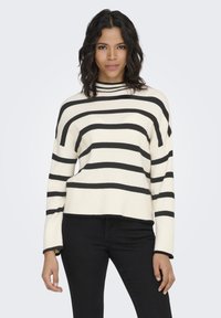 Cream sweater with black horizontal stripes, ribbed texture, high neck, and wide bell sleeves, paired with black pants.