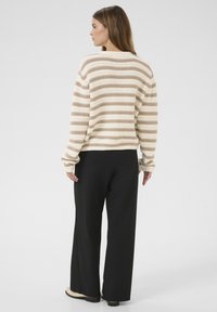 Crème en beige gestreepte gebreide trui met een relaxed fit en lange mouwen, gecombineerd met zwarte wijde broek en zwarte schoenen.