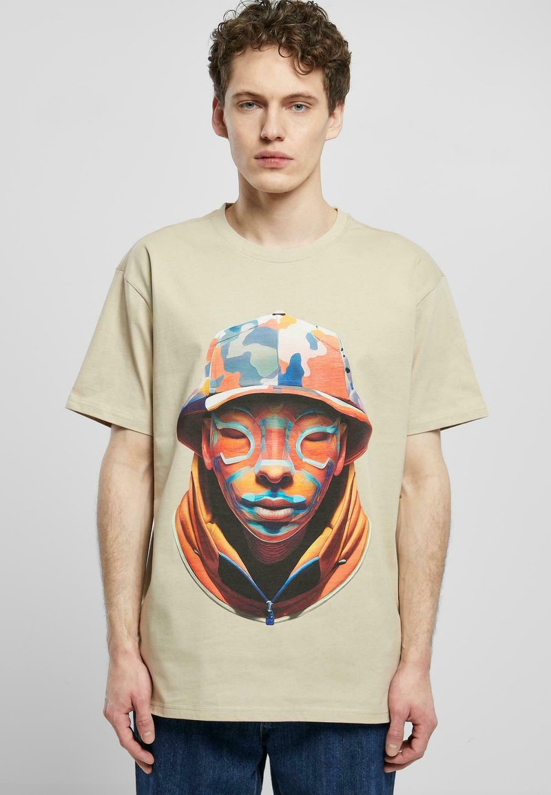 Beige bomull t-shirt med en färgglad grafik av ett ansikte med en detaljerad, mönstrad hatt och en orange huva. Lös passform med korta ärmar.