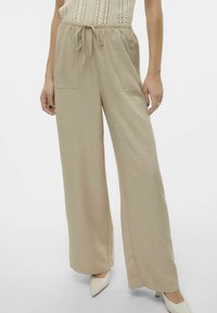 Pantalons beige à jambes larges avec une taille élastique à cordon, deux poches avant et une texture lisse, associés à des talons aiguilles crème.