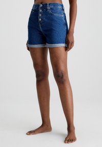 Shorts in denim di colore blu scuro con vita alta, chiusura a cinque bottoni e orli arrotolati. Texture liscia con dettagli di cucitura discreti.