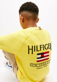 Felpa di cotone gialla con ricamo della scritta "HILFIGER" e patch con logo sul retro. Presenta polsini e orlo a costine.