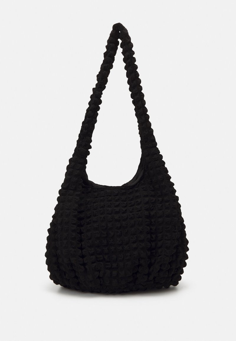 Sac à main noir en tissu texturé façon gaufré avec une large bandoulière, présenté sur un fond clair uni.