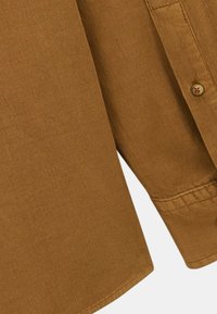 Chemise marron côtelée avec fermeture à boutons. Elle dispose d'un col et de poignets, présentant une texture lisse et un design structuré.