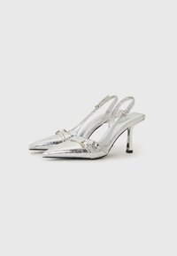 Stříbrné slingback podpatky s špičatou špičkou, s lesklým metalickým povrchem a malým páskem vpředu. Umírněný jehlový podpatek.