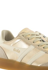 Gola-sneaker med ett guldfärgat metalliskt övre, vita detaljer, grå mockadetaljer och ljusgrå snören. Gummisul med strukturerad yta.