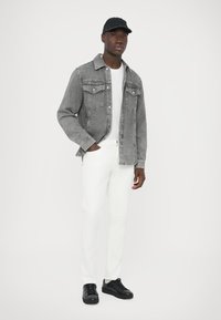 Siva denim jakna, bela majica, bele hlače in črni superge. Jakna ima dva prsna žepa, kapa pa je mornarsko modra.