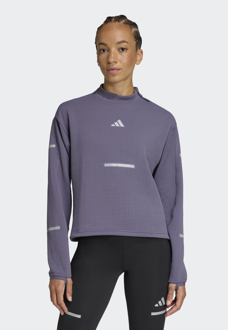 Top deportivo de manga larga texturizado en púrpura con acentos reflectantes y el logo de Adidas. Combinado con leggings negros.