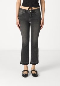 Sorte denim flared jeans med en rå kant, fem lommer og knaplukning. Kombinert med sorte stroppesko.