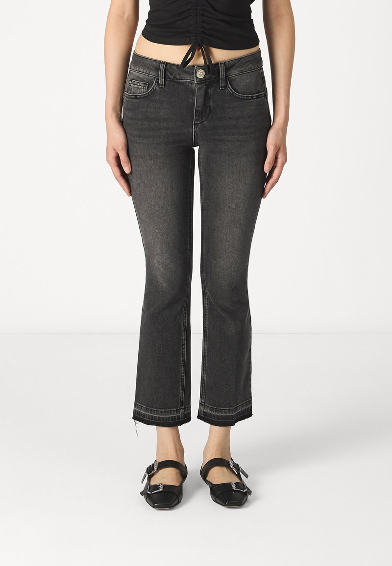 Sorte denim flared jeans med en rå kant, fem lommer og knaplukning. Kombinert med sorte stroppesko.