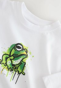 Weißes Baumwoll-T-Shirt mit einem grünen Cartoon-Frosch-Design, umrahmt von schwarzen Linien und Spritzern in Gelb und Grün drumherum.