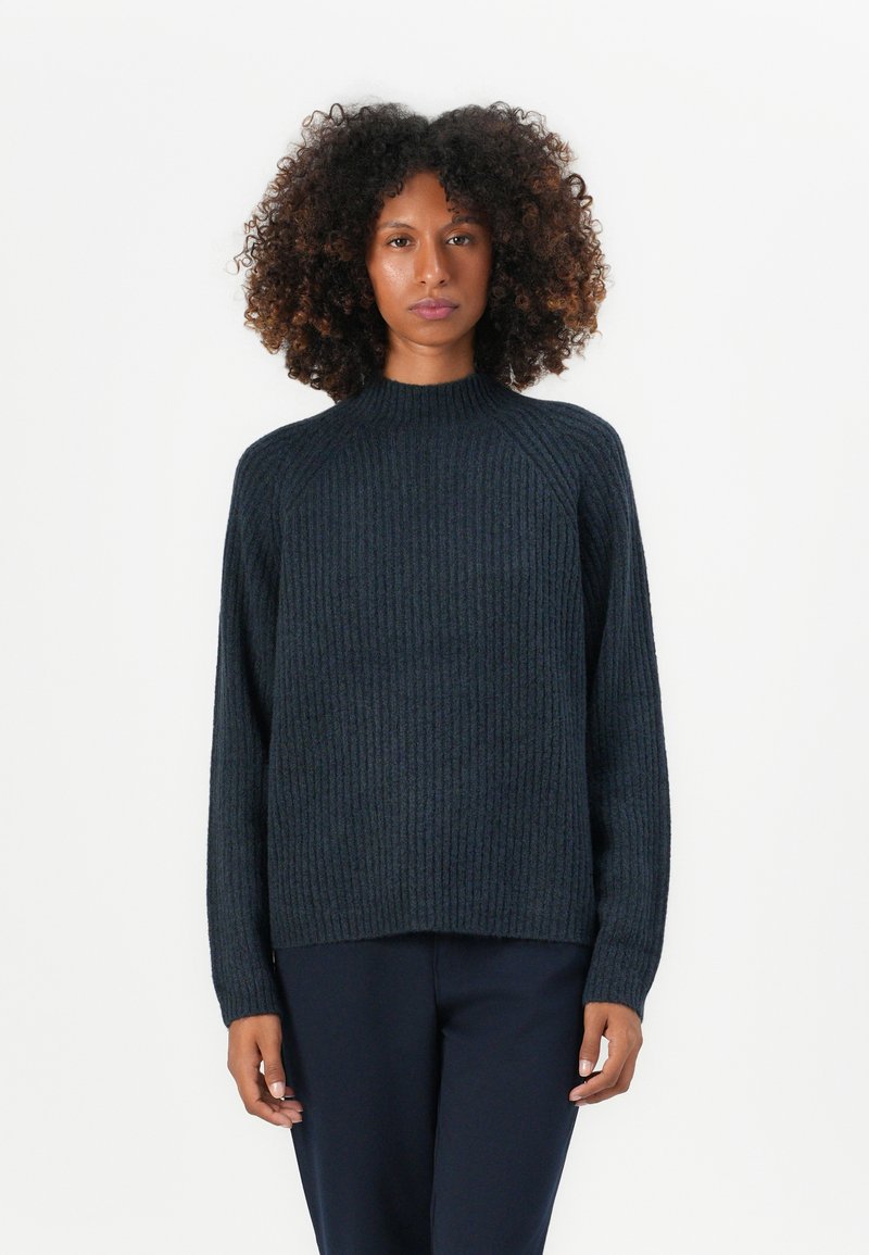 Pulover din tricot cu dungi, de culoare bleumarin închis, cu guler înalt și mâneci raglan, având o croială lejeră și o textură moale. Pantalonii sunt bleumarin.