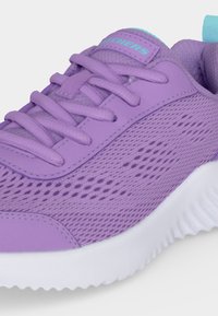 Gros plan sur une chaussure de sport lavande à texture en mesh, lacets assortis et semelle blanche épaisse, montrant les détails latéraux et avant.