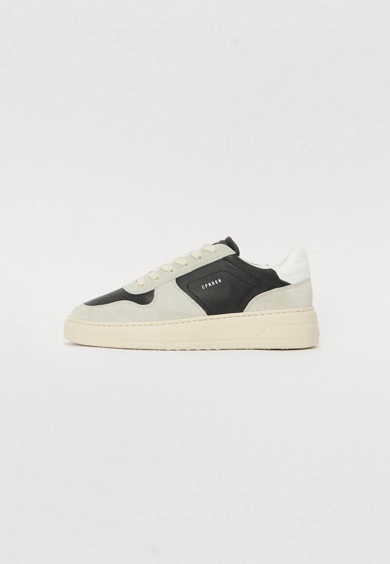 Die Sneaker bestehen aus einer Kombination von schwarzem Leder und hellgrauem Wildleder mit einer strukturierten Oberfläche. Die Sohle und die Schnürsenkel sind aus cremefarbenem Gummi, mit einer Markenkennzeichnung an der Seite.