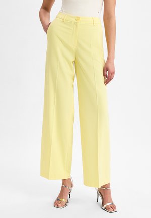 Heldere gele wijde broek met een gladde textuur, hoge taille, zijzakken en een enkele knoopsluiting aan de voorkant. Gecombineerd met metallic hakken.