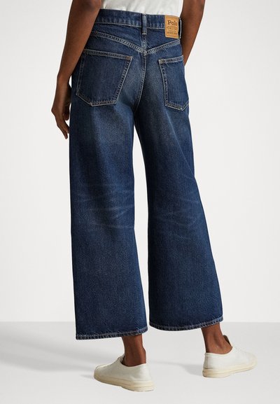 Μπλε παντελόνια τζιν σε φαρδιά γραμμή, κατασκευασμένα από ντένιμ, με ψηλή μέση, μεγάλα πίσω τσέπες και ένα καφέ λογότυπο. Λείο υλικό με κλασική εφαρμογή.