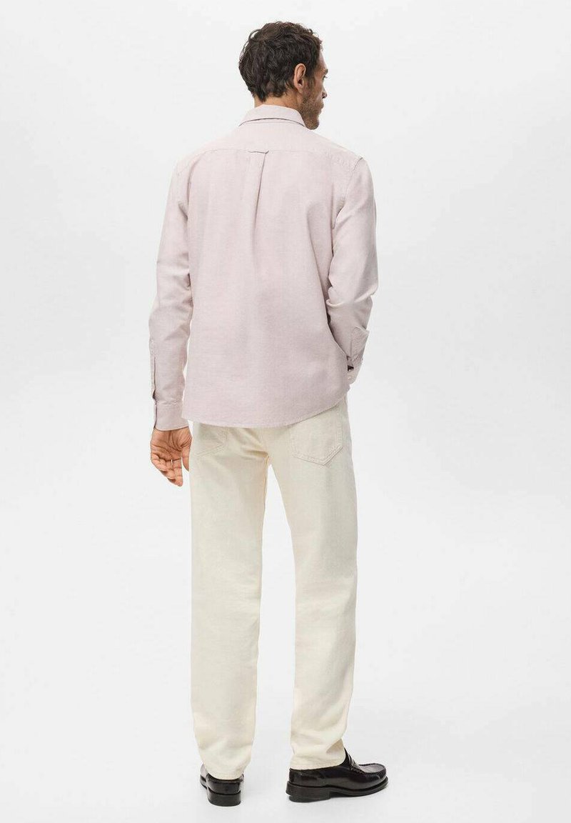 Camicia rosa chiaro con maniche lunghe e piega posteriore. Abbinata a pantaloni color crema e scarpe nere. Design semplice, senza motivi visibili.