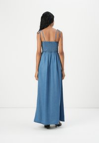 Denim maxi-kjole med en tettsittende smocked liv og justerbare stropper. Stoffet er i en lys blå nyanse med en jevn tekstur.