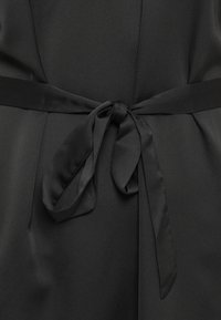Ceinture en tissu noir nouée en un joli nœud autour de la taille d'un vêtement, avec un matériau lisse et légèrement texturé visible.
