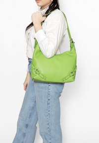Sac en cuir vert au toucher doux, avec des accents en métal argenté et une silhouette décontractée, porté à l'épaule.